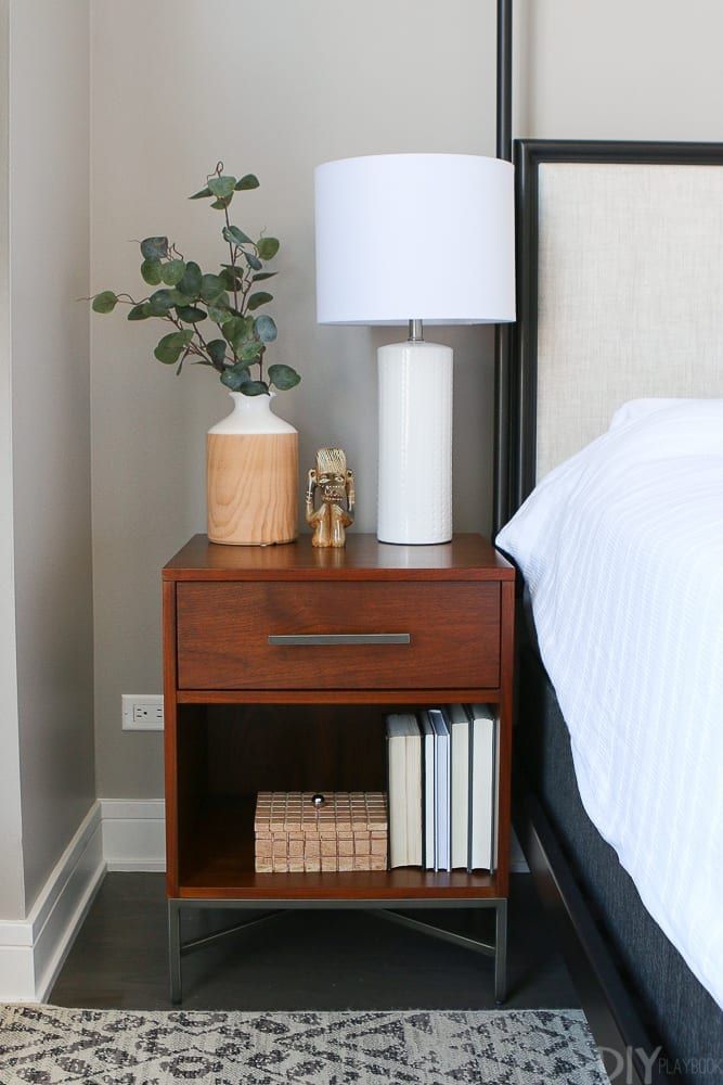 a nightstand with books and a lamp on it next to a bed in a bedroom