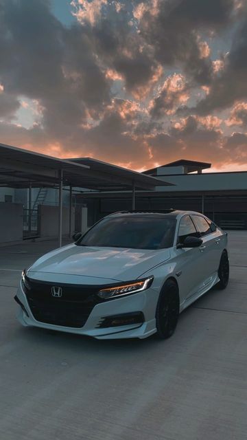 a white car parked in front of a building with clouds above it and the sun going down