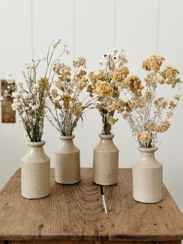 three white vases with dried flowers in them