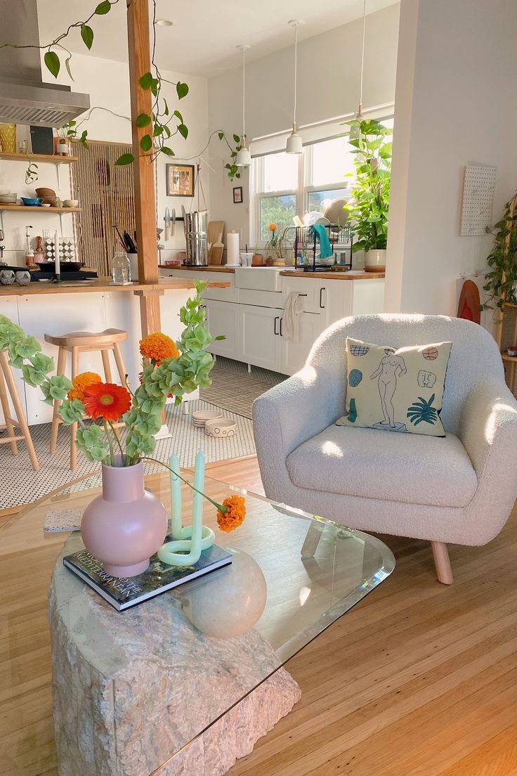 a living room filled with furniture and flowers on top of a coffee table in front of a kitchen