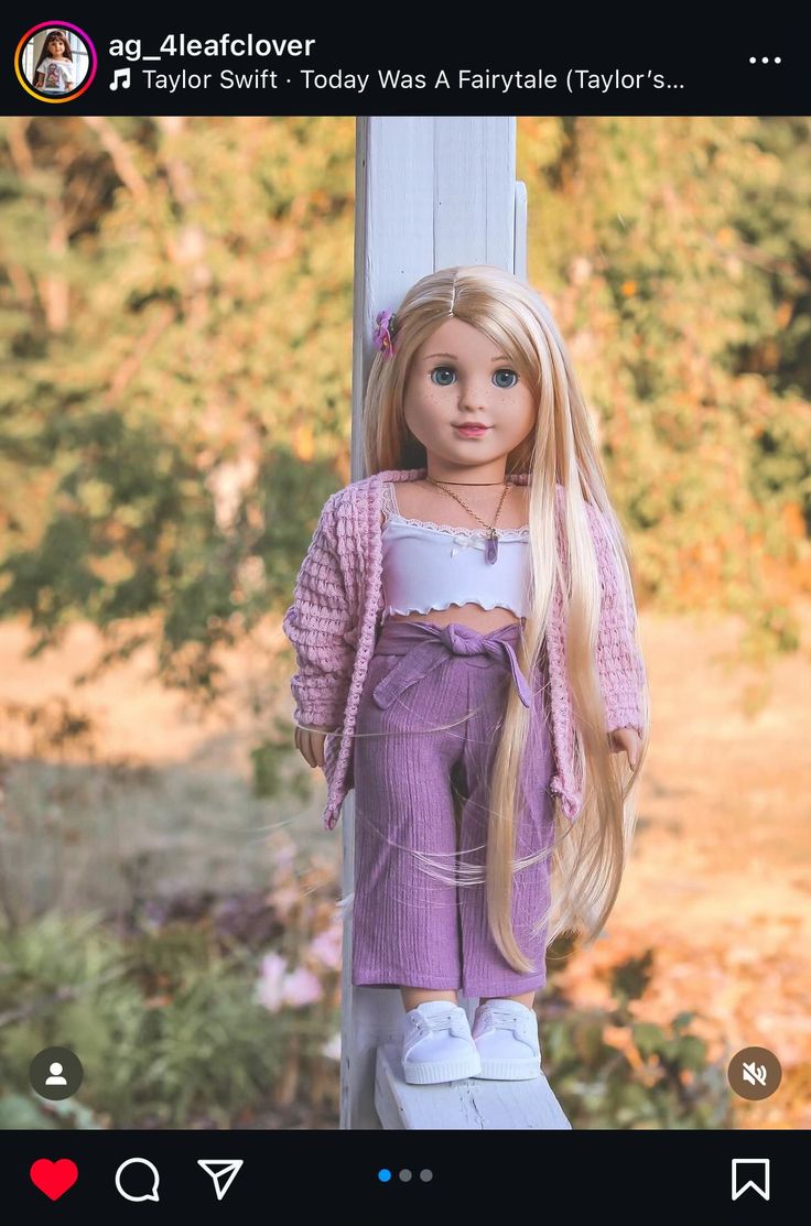 a doll with long blonde hair standing next to a white pole in front of trees