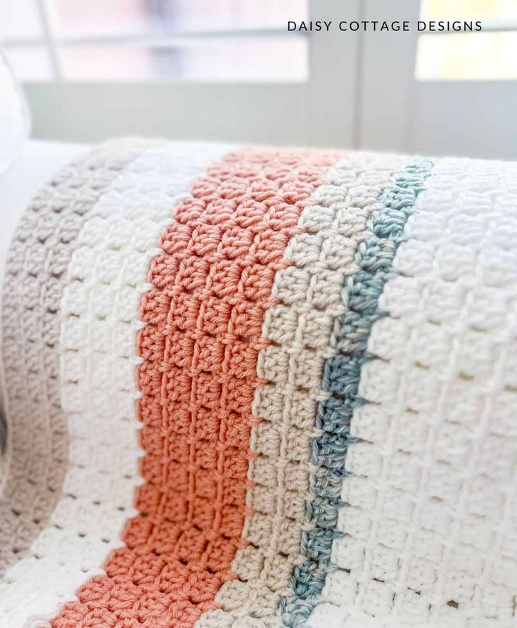 a crocheted blanket sitting on top of a white couch next to a window