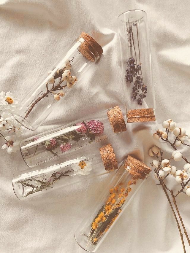 four glass bottles with dried flowers in them on a white cloth covered tablecloth,