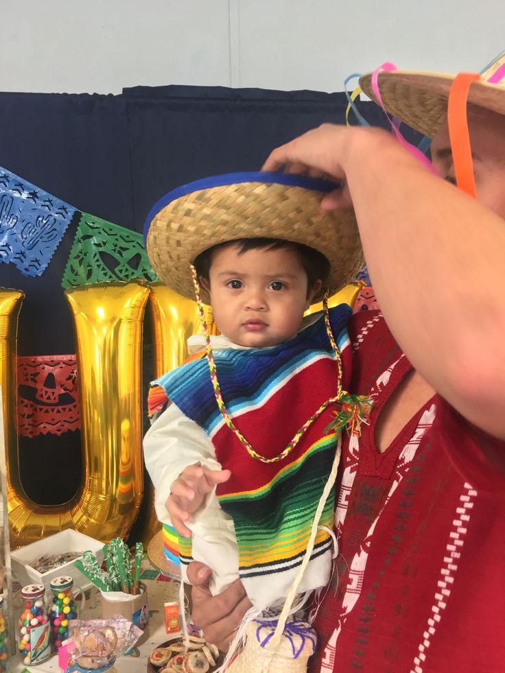 a young child wearing a mexican hat and holding an adult's hand over his shoulder