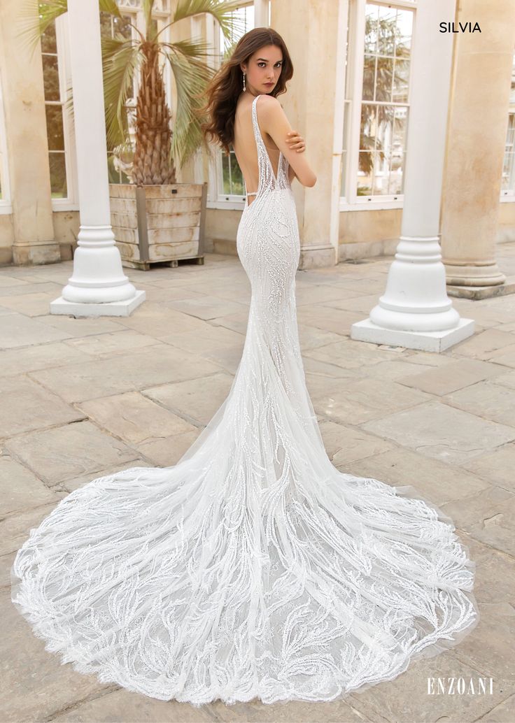 a woman in a white wedding dress standing on a stone walkway with columns and palm trees behind her