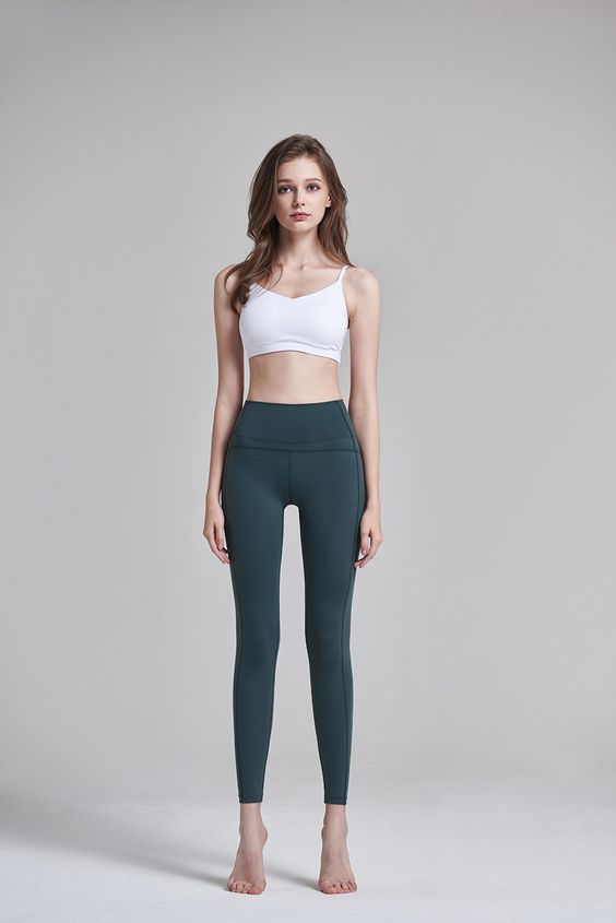 a woman in green leggings and a white top is posing for the camera