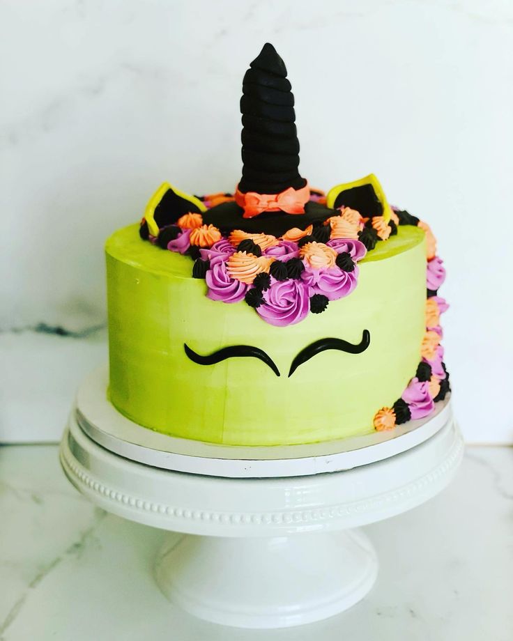 a green cake decorated with flowers and a unicorn's horn on top is sitting on a white pedestal