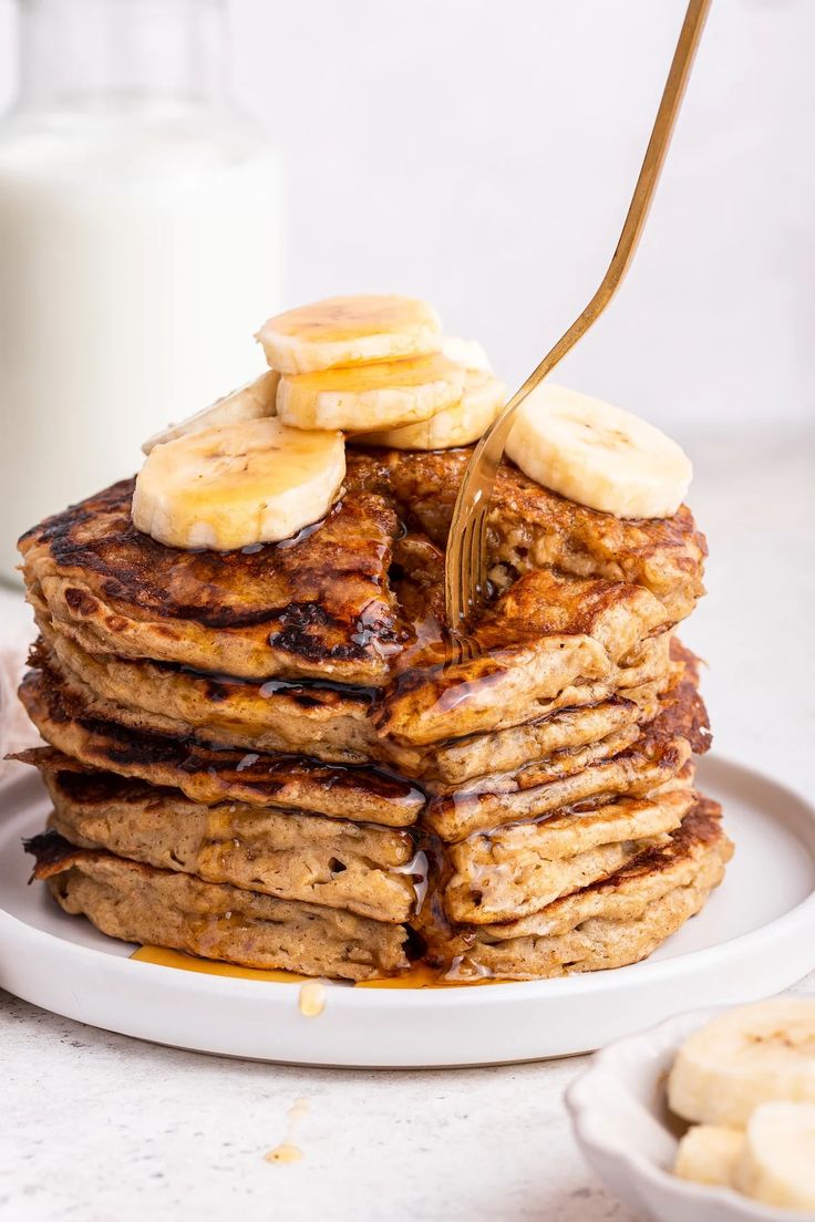 a stack of pancakes with bananas and syrup on a plate next to a glass of milk