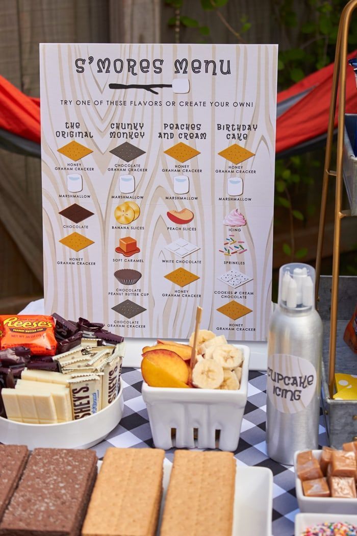 a table topped with lots of desserts next to a sign that says s'mores menu