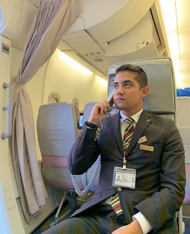 a man in a suit sitting on an airplane talking on a cell phone while holding his hand up to his ear