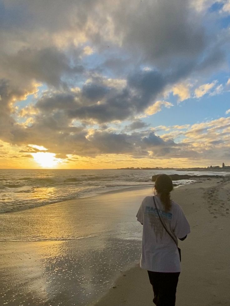 a woman is walking along the beach at sunset