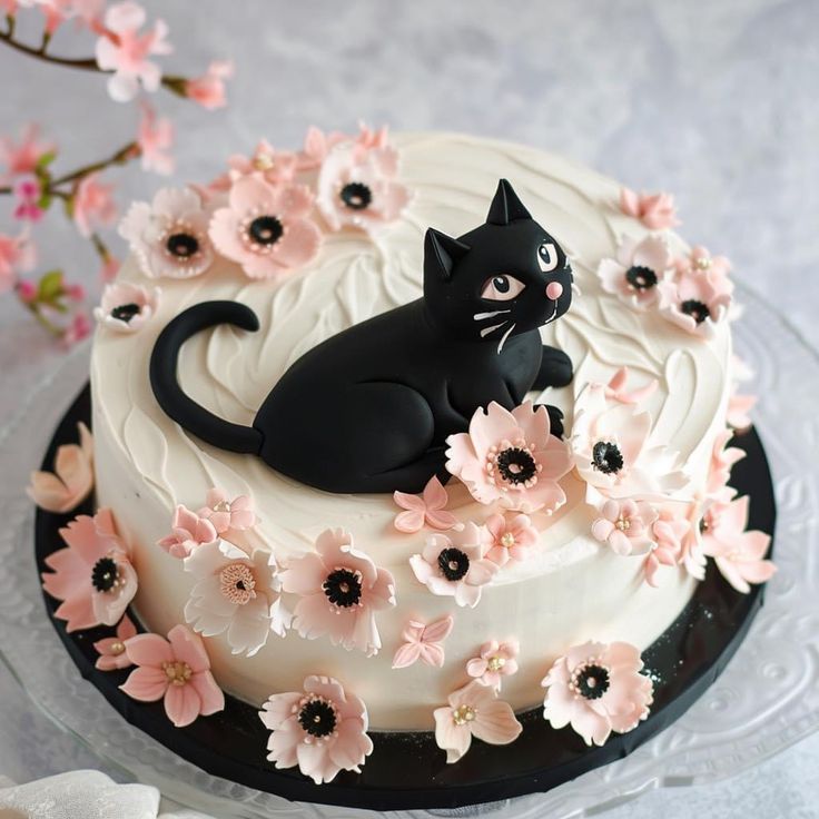 a black cat sitting on top of a white cake covered in pink and purple flowers