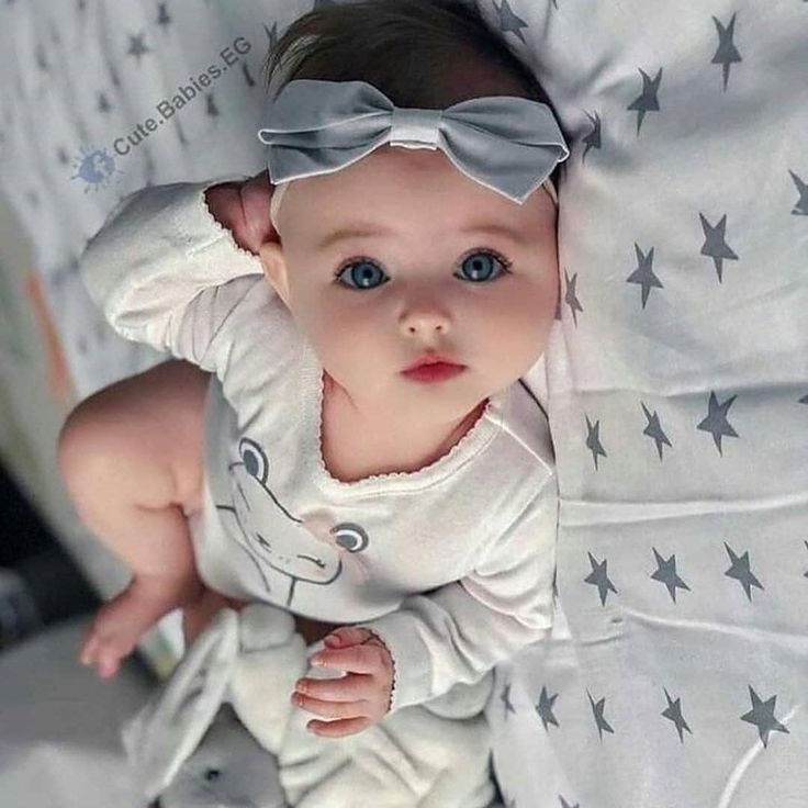 a baby laying on top of a bed wearing a white shirt and gray bow tie