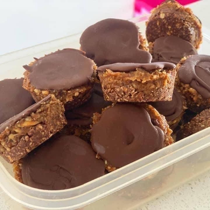 a container filled with chocolate covered desserts on top of a white countertop next to a pink flower