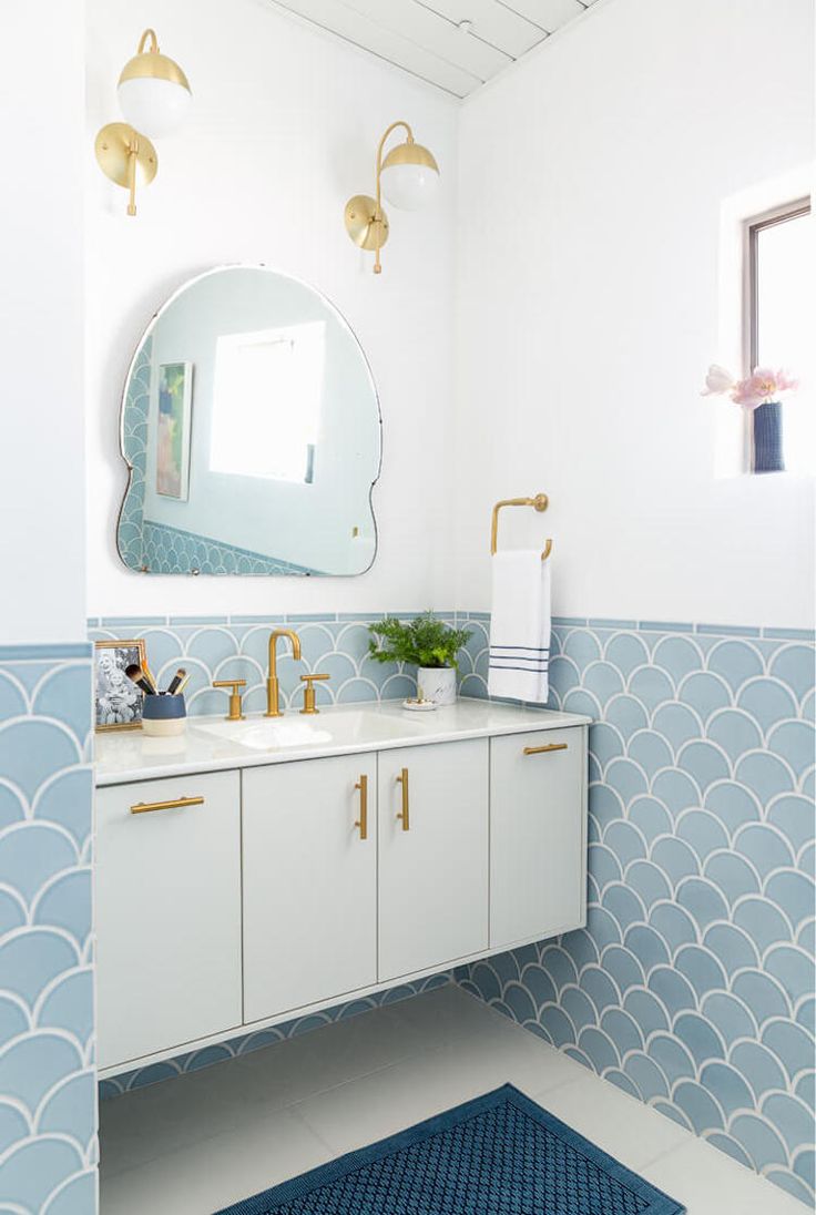 a bathroom with blue and white tiles on the walls, gold faucets and a large round mirror