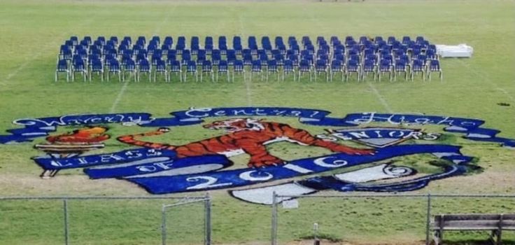 a large blue and white sign on top of a grass covered field next to benches