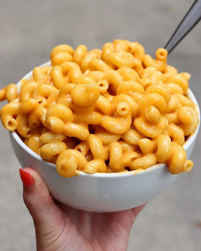 a hand holding a white bowl filled with macaroni and cheese