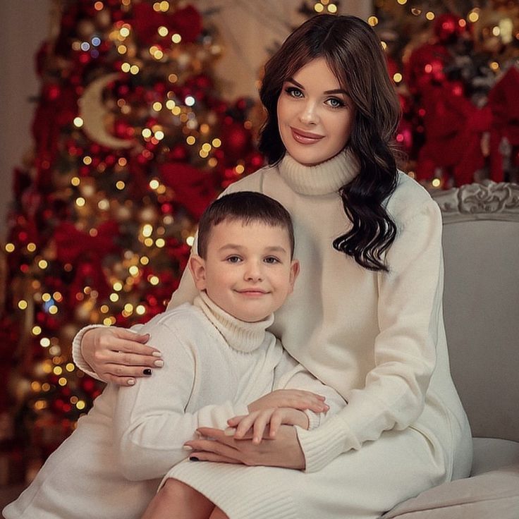 a woman sitting next to a boy in front of a christmas tree