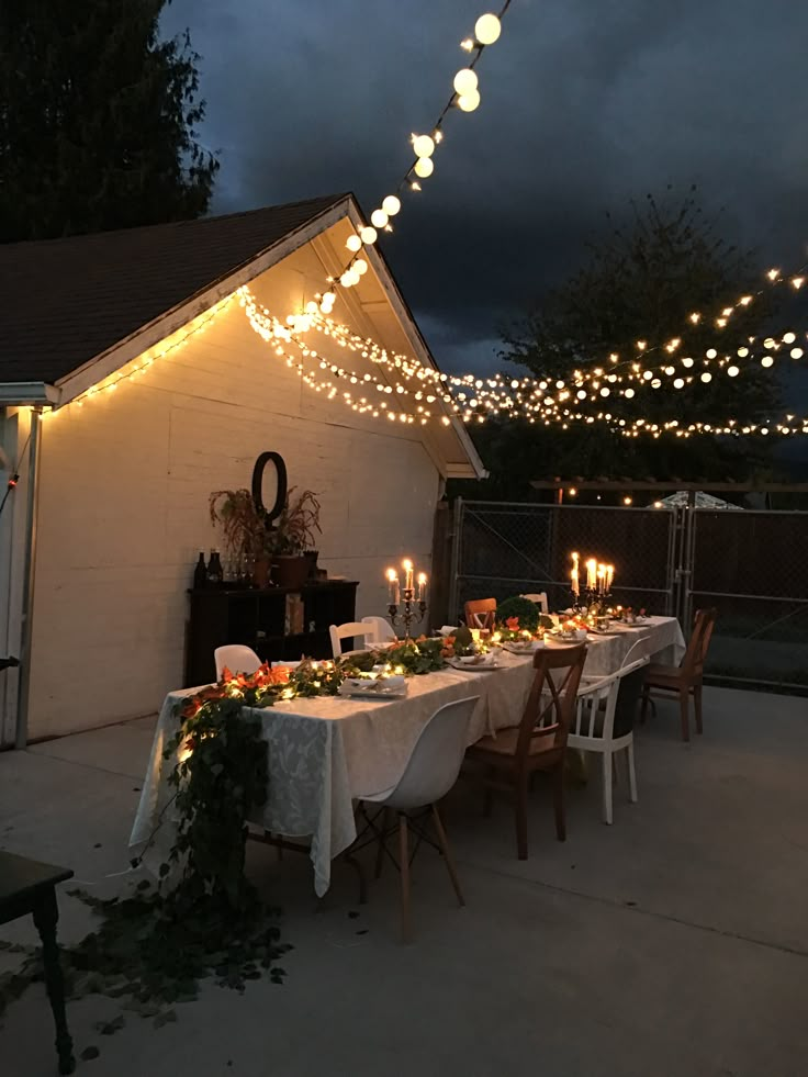 an outdoor dining table set up with candles and greenery on the table for dinner