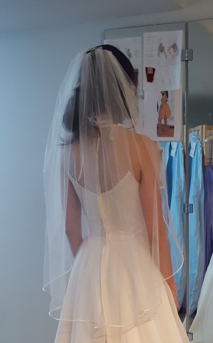 the back of a bride's wedding dress as she stands in front of a mirror