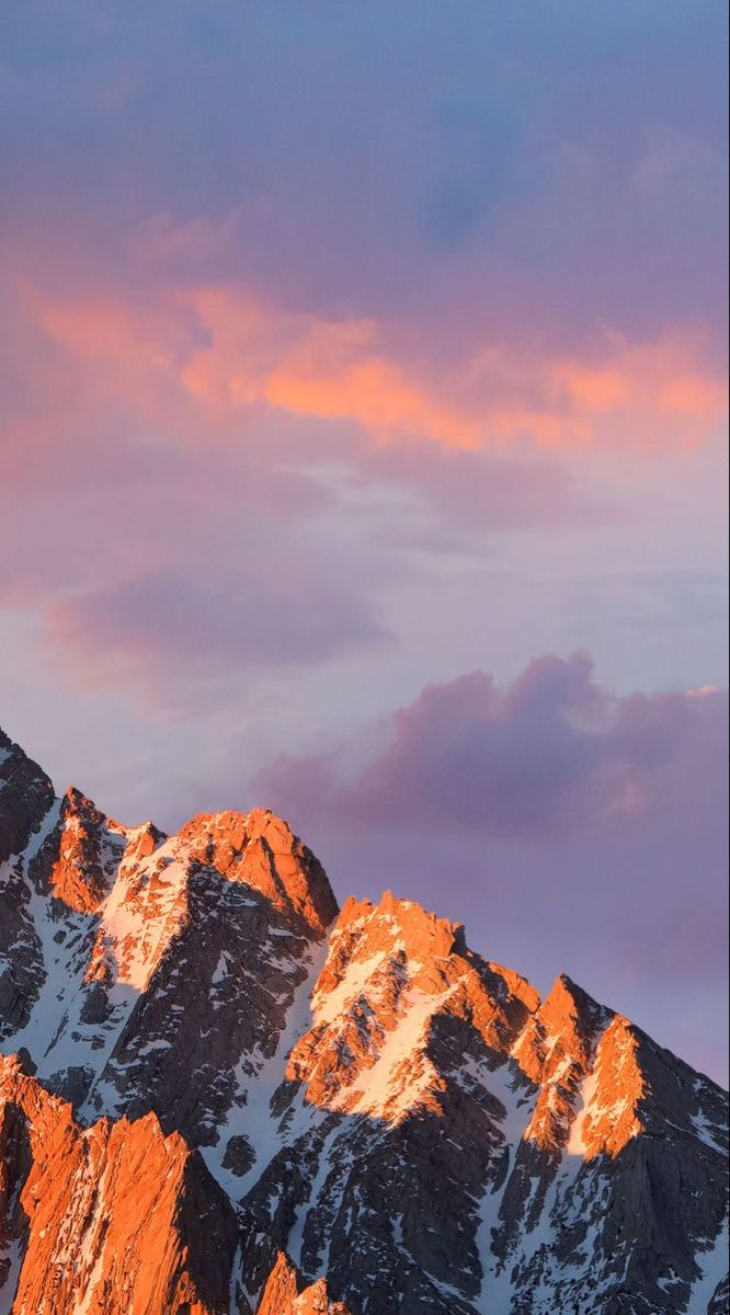 the mountains are covered in snow and pink clouds at sunset or sunrise, as seen from below