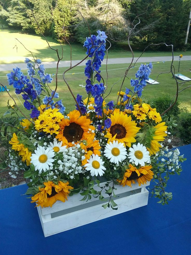 an arrangement of flowers in a white vase on a blue table cloth with trees in the background