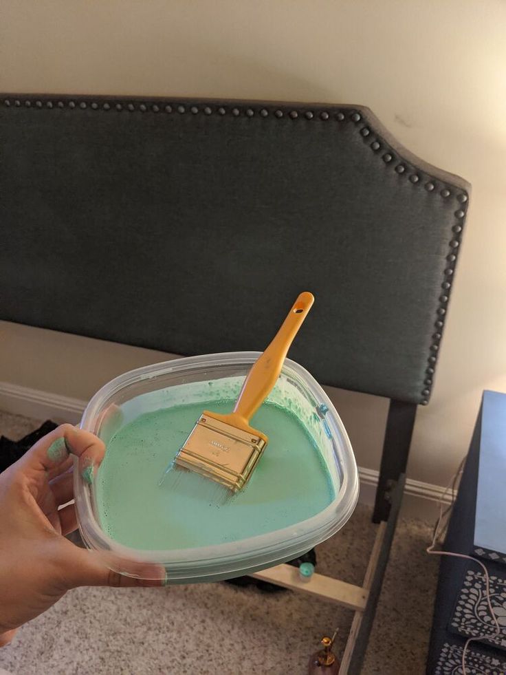 a person is holding a paintbrush in a container with green liquid on the floor