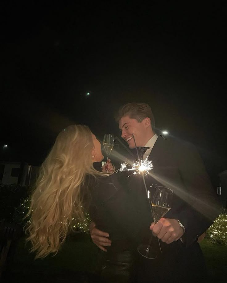 a man and woman standing next to each other at night with sparklers in their hands