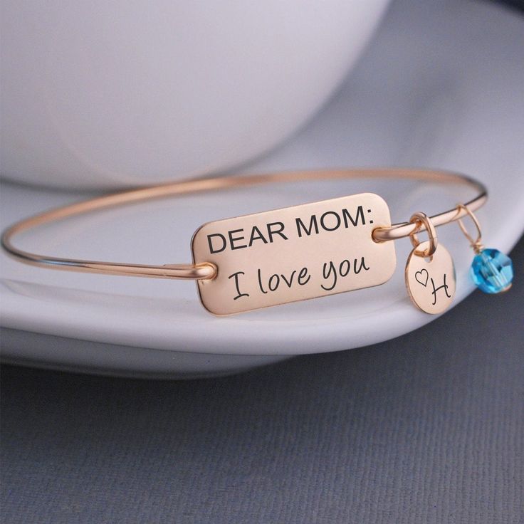 A stainless steel rectangle measuring 1 inch across is engraved with "DEAR MOM: I love you". Each bangle is hand formed from sterling silver wire, then hammered and tumbled for shine and strength. Bracelets are available in 14k gold filled and 14k rose gold filled. All charms are optional. Choose from 3/8 inch initial charms (they include the heart on them as shown) 6mm Swarovski crystal birthstone charms Note: Our bangle bracelets do not have clasps and they slide over the hand. Use the Bangle Custom Bangle, Personalised Bangle, Bracelet Size Chart, Graduation Jewelry, The Bangles, Rose Gold Charms, Dear Mom, Yoga Jewelry, Gold Bangle Bracelet