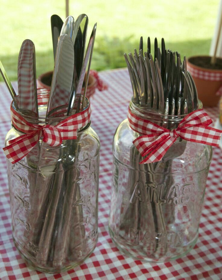 two mason jars with forks and spoons in them sitting on a checkered table cloth