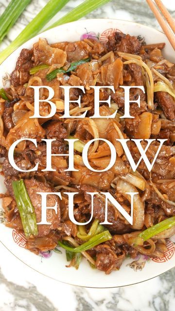 beef chow fun on a white plate with chopsticks and green onions next to it