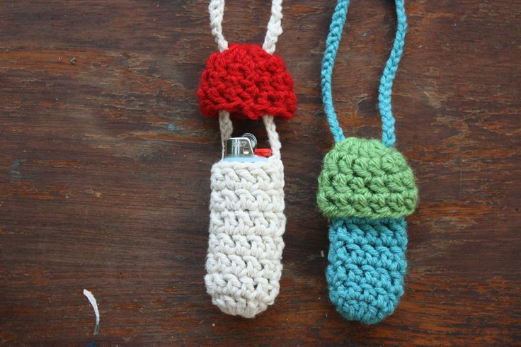 two crocheted items hanging from strings on a wooden surface, one is red and the other is blue