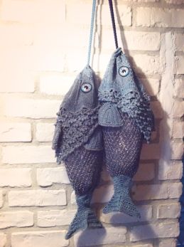 two knitted fish hanging from hooks on a brick wall