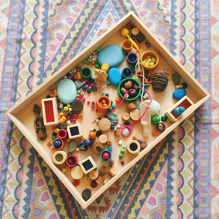 a wooden tray filled with toys on top of a colorful table cloth covered in multicolored fabric