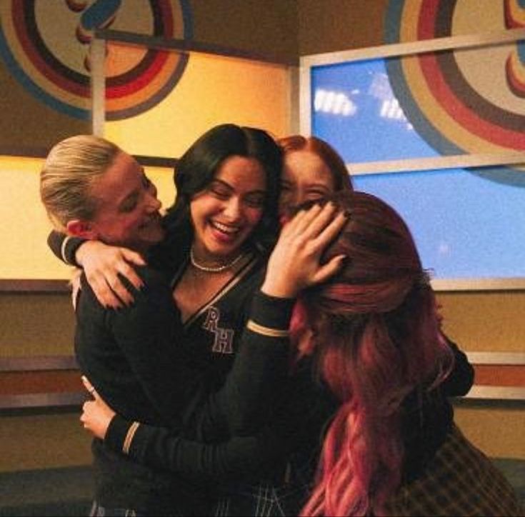 three people hugging each other in front of a wall with colorful circles on the background