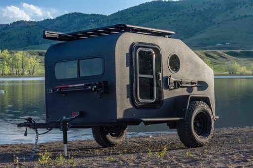 an off - road camper parked on the shore of a lake