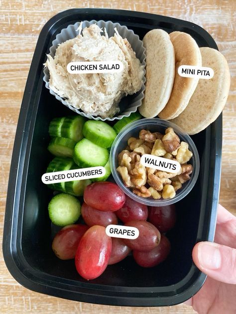 a black tray with grapes, crackers, hummus, and other food items