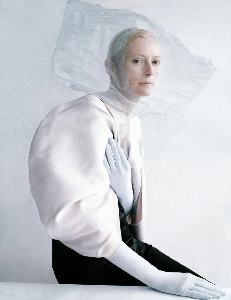 a woman with white hair and gloves on her head sitting in front of a white background