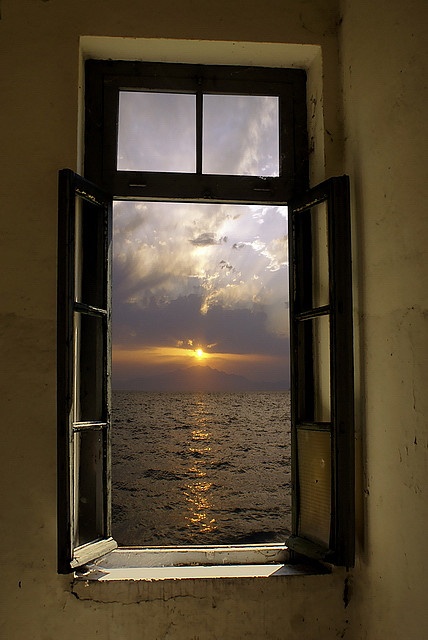 an open window with the sun setting over the ocean in front of it on a cloudy day