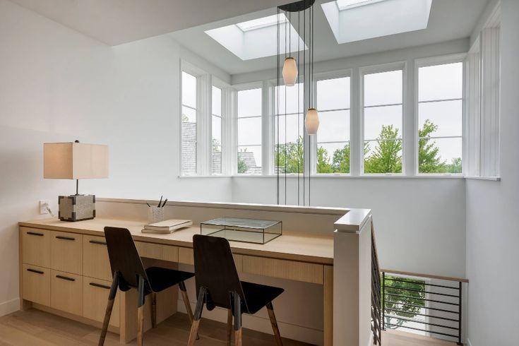 two chairs are sitting at a desk in the middle of a room with large windows