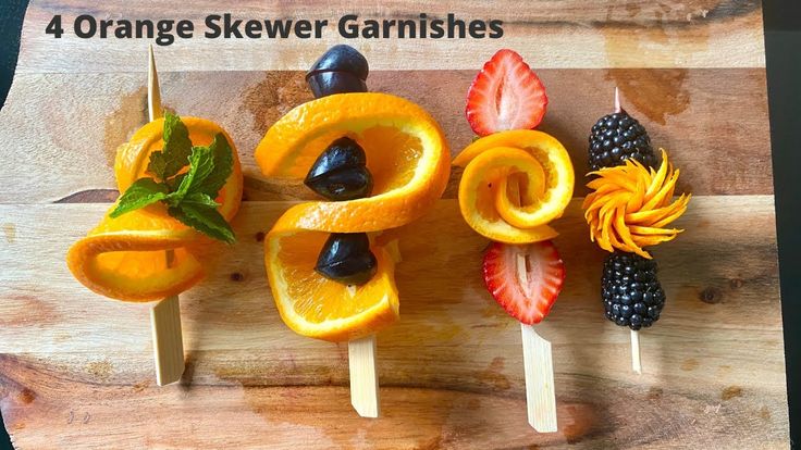 four orange skewer garnishes with fruit on them