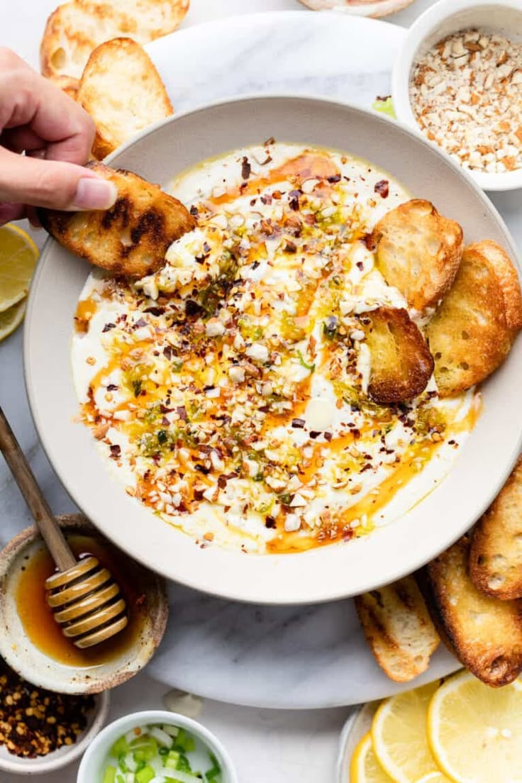 a bowl of hummus with toasted bread on the side and lemon slices around it