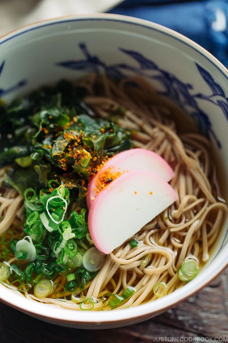 a bowl filled with noodles and vegetables on top of a wooden table