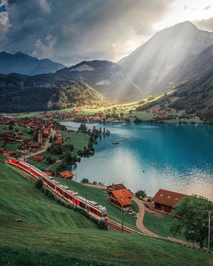 a train traveling down tracks next to a body of water with mountains in the background