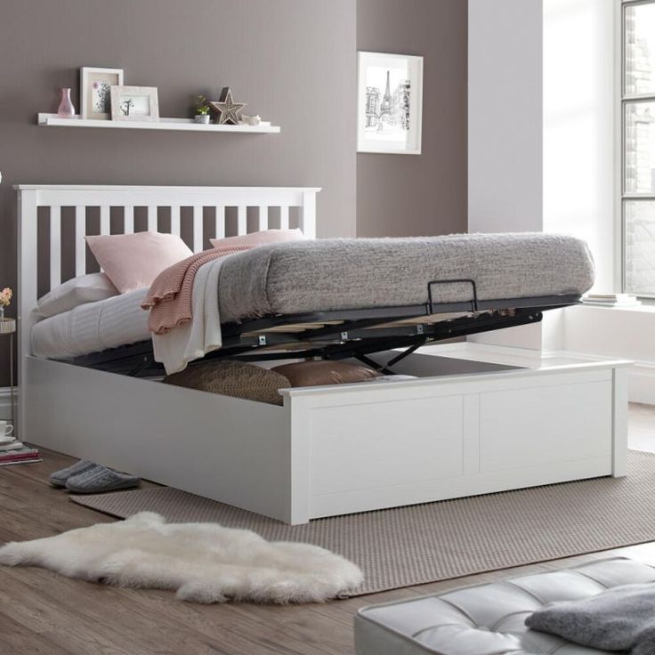 a white bed with a pull out storage box underneath it in a living room next to a window