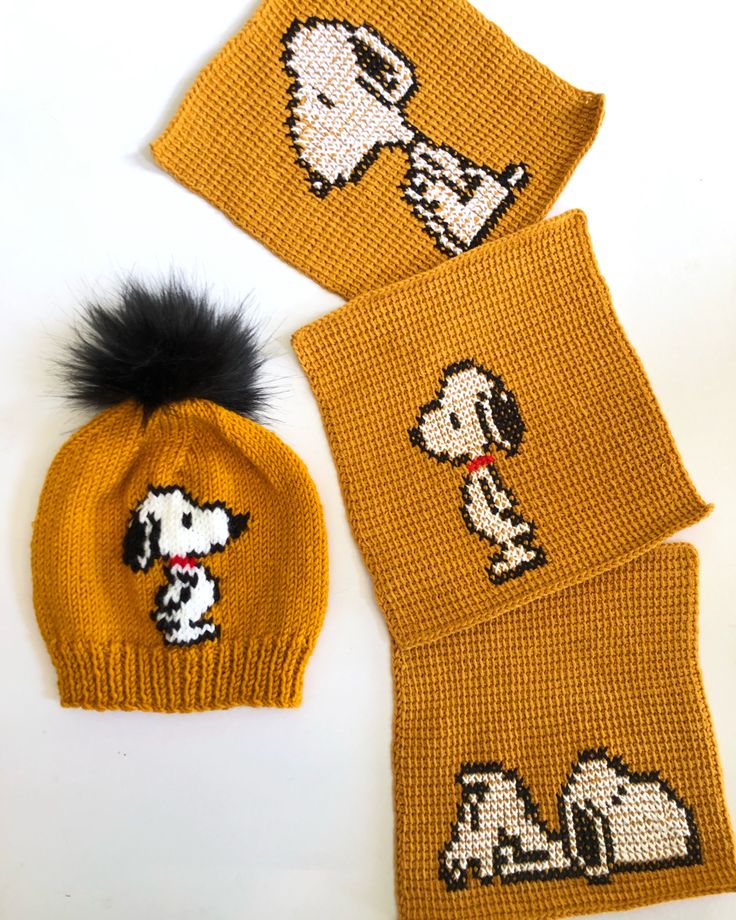 two knitted beanies, one with a dog on it and the other has a black pom - pom