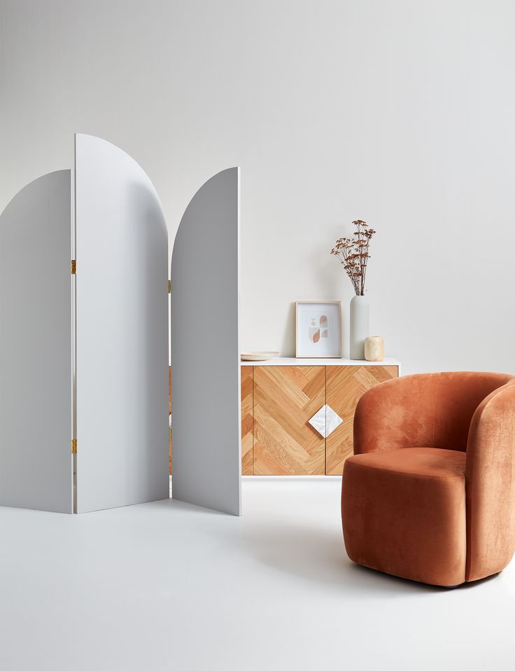 an orange chair sitting in front of a white wall next to a wooden cabinet with two doors