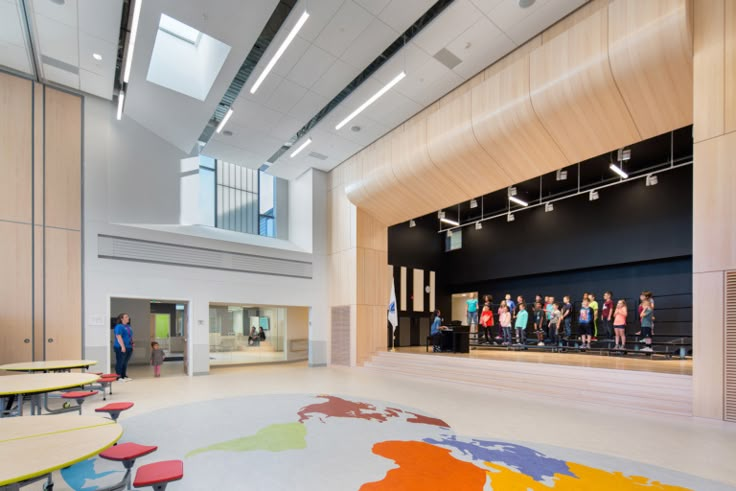 an empty room with tables and chairs in it, people are standing on the stage