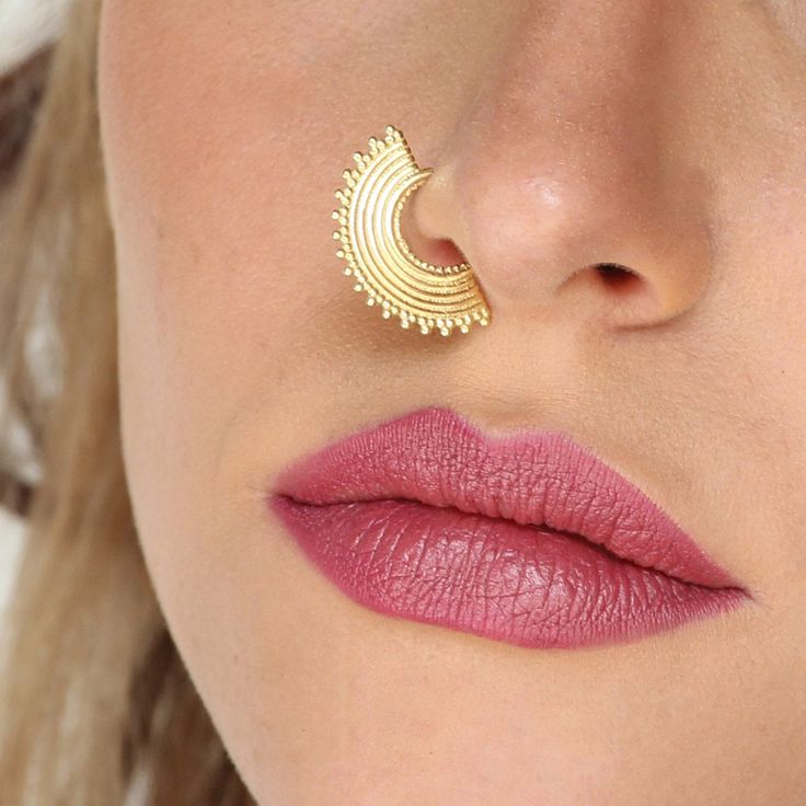 a close up of a woman's nose with a gold nose pin in the shape of a crescent