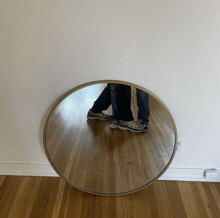 a person standing in front of a mirror on top of a wooden floor next to a wall